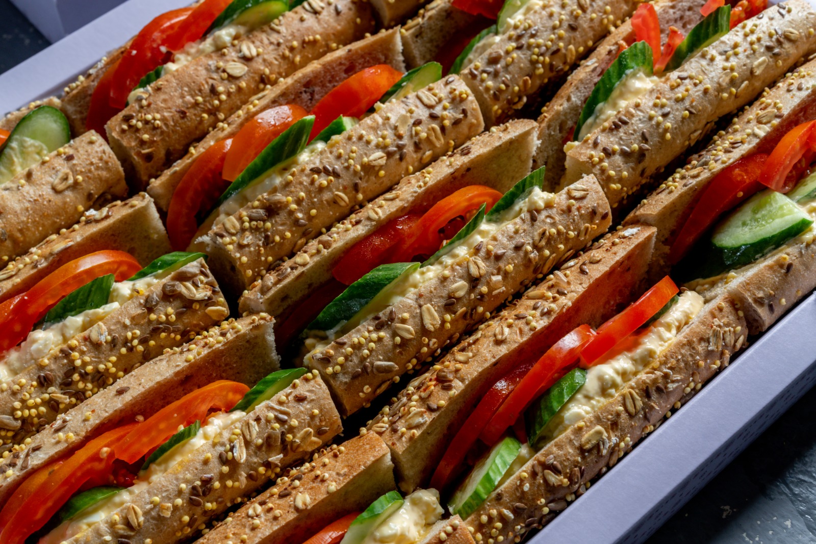 A tray of egg salad and fresh vegetables sandwiches on grains flute